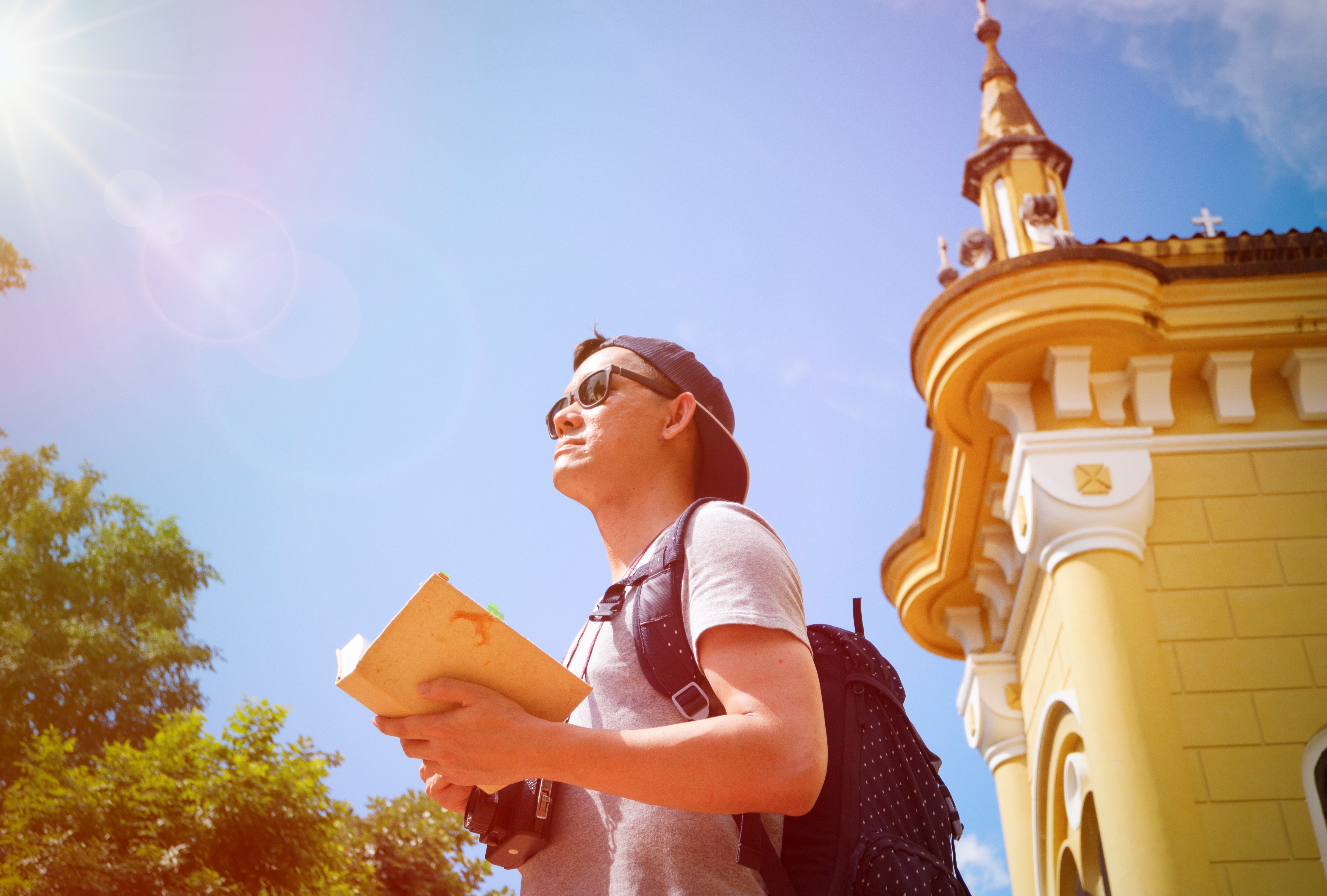 young man traveler with a backpack on his shoulder out sightseeing with the guide book , travel and recreation concept